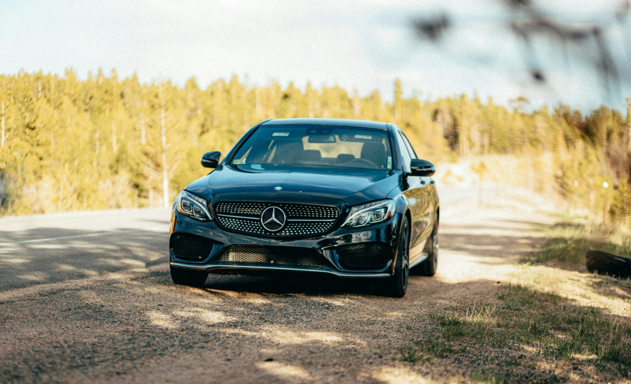 Black Mercedes-Benz sedan parked on a rural forest road in sunlight